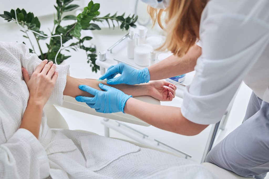 A nurse carefully prepares a patient's arm for IV Therapy, ensuring comfort and precision during the process at Revive & Drip in Washington, PA. This detailed image showcases the attentive care provided by the medical professionals at Revive & Drip, where IV Therapy is tailored to meet the unique needs of each client. IV Therapy at Revive & Drip not only delivers hydration and essential nutrients directly into the bloodstream but also complements a wide range of other treatments offered by the clinic, including Botox, fillers, aesthetic treatments, and weight loss programs. The image highlights the meticulous preparation that goes into each treatment, emphasizing the clinic’s commitment to delivering safe, effective, and rejuvenating health and beauty solutions to every client.