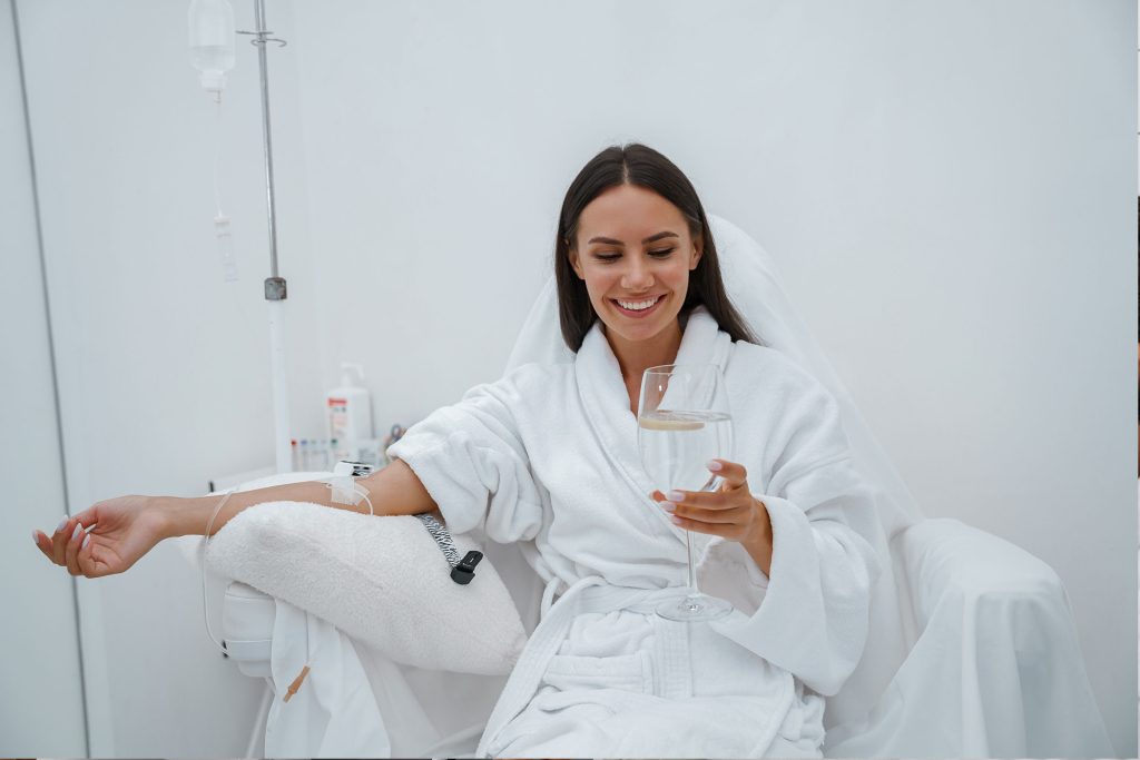 A beautiful woman in a white robe sits comfortably in a recliner, receiving an IV Infusion at Revive & Drip in Washington, PA. The serene environment highlights the relaxing experience of IV Therapy, designed to rejuvenate and refresh the body with essential nutrients and hydration. This image encapsulates the essence of luxury and wellness that Revive & Drip offers through their comprehensive range of treatments, including Botox, fillers, aesthetic treatments, and personalized weight loss programs. The soothing ambiance and professional care provided during IV Therapy make it an ideal choice for those looking to enhance their health and beauty effortlessly.