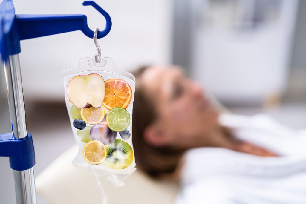 An IV bag filled with vibrant fruit, symbolizing the nourishing ingredients of Magnetize IV Therapy, is shown alongside a woman in a white robe comfortably reclining while receiving her treatment at Revive and Drip. The setting highlights the calming and rejuvenating experience offered by Revive and Drip, where a range of services including IV Therapy, Botox, fillers, aesthetic treatments, and personalized weight loss solutions are provided to enhance overall wellness and natural beauty.