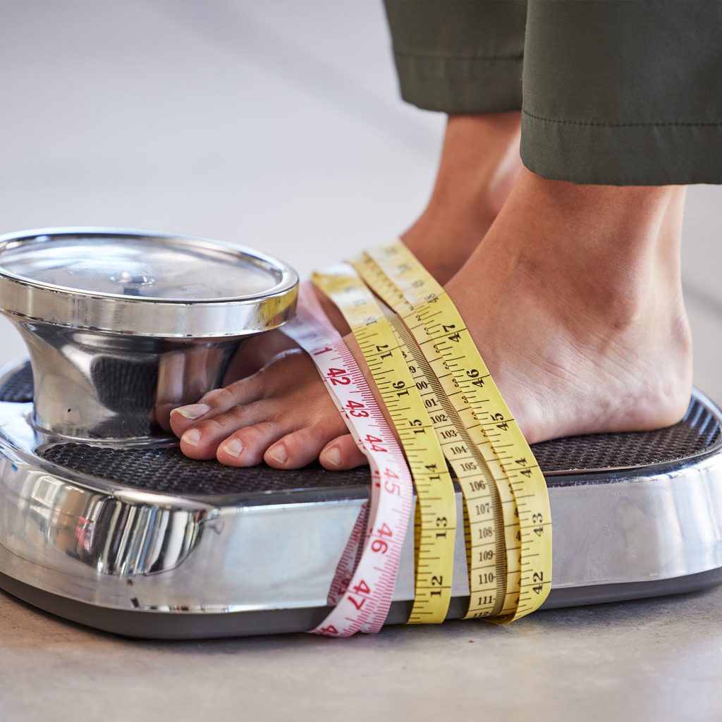 A woman standing on a scale with measuring tape around her feet, symbolizing weight loss progress and the use of Semaglutide for weight management.